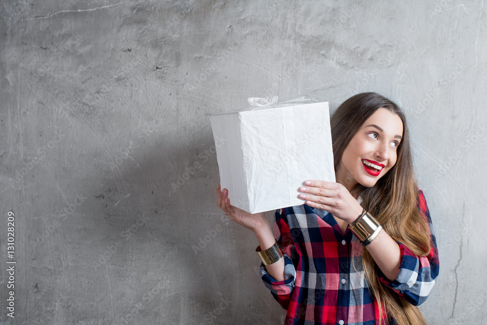 Young woman holding white gift box on the gray wall background