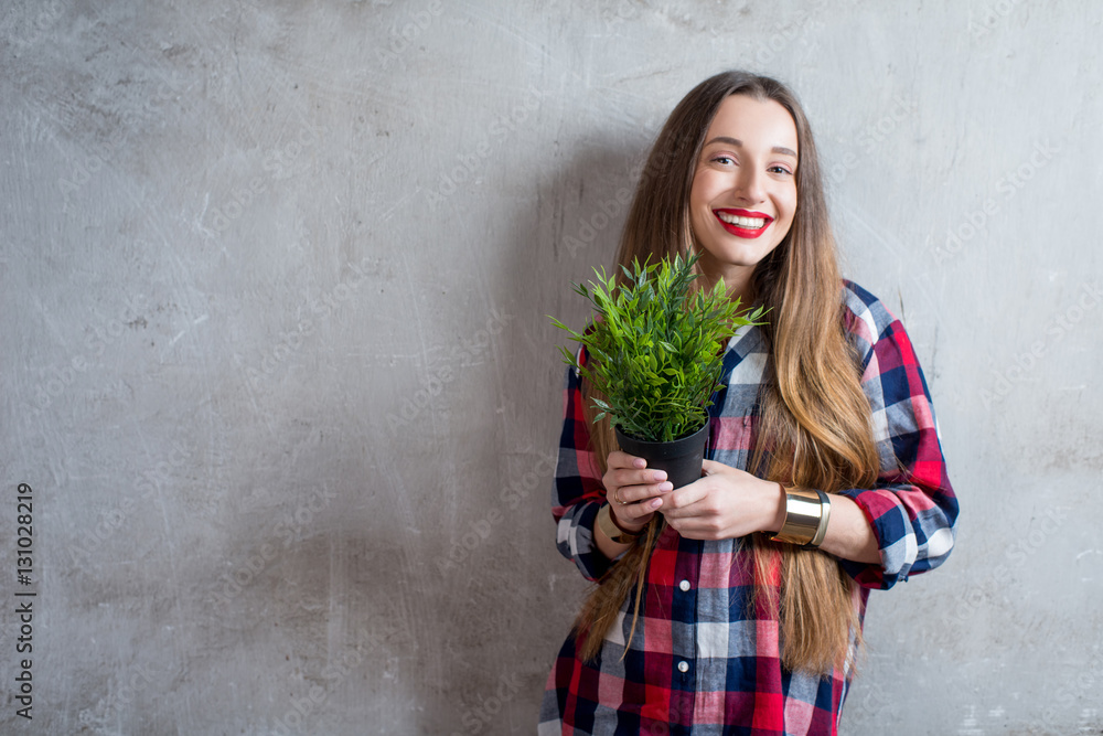 Young woman in checkered shirt with flowerpot on the gray wall background