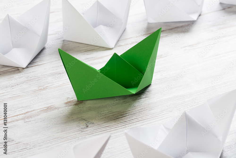 Business leadership concept with white and color paper boats on wooden table