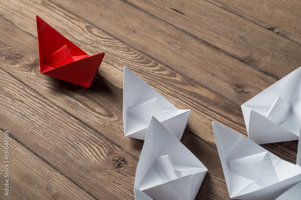 Business leadership concept with white and color paper boats on wooden table