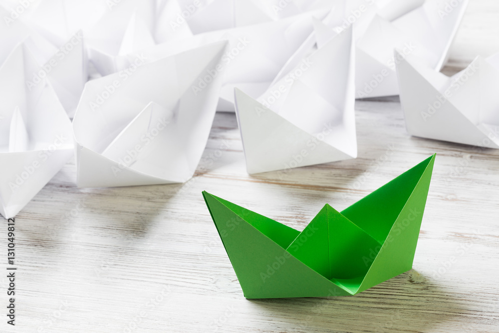 Business leadership concept with white and color paper boats on wooden table