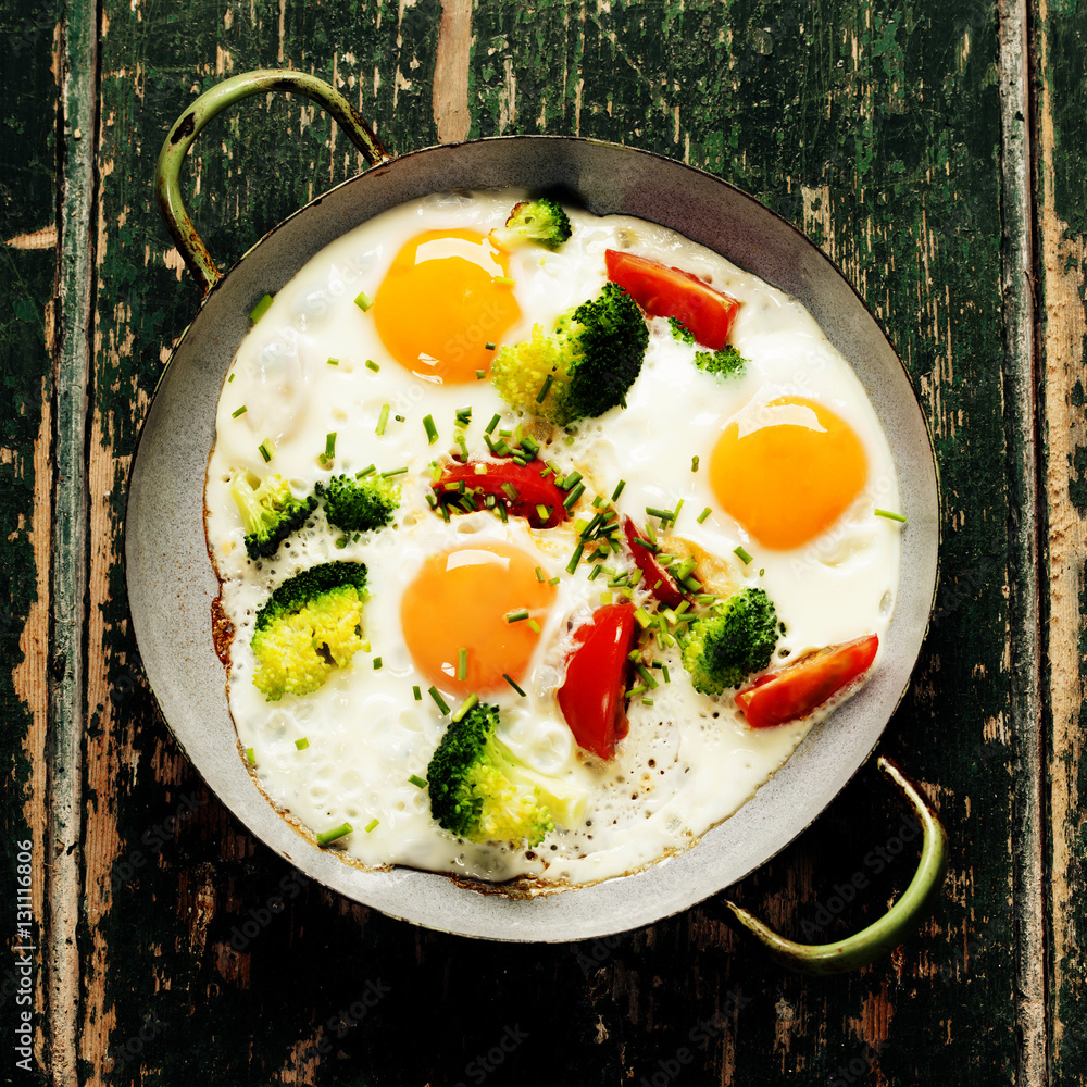 Pan of fried eggs, broccoli and cherry-tomatoes, top view