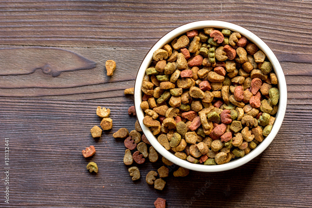 dry cat food in bowl on wooden background top view