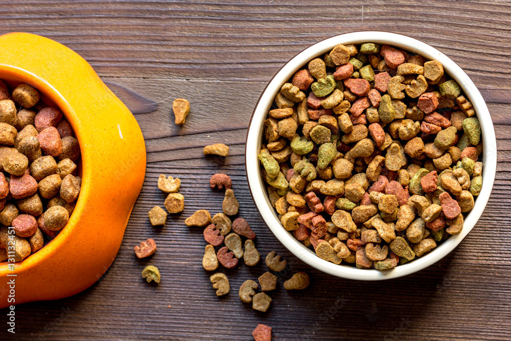 dry cat food in bowl on wooden background top view