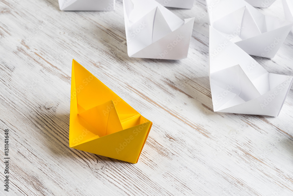 Business leadership concept with white and color paper boats on wooden table