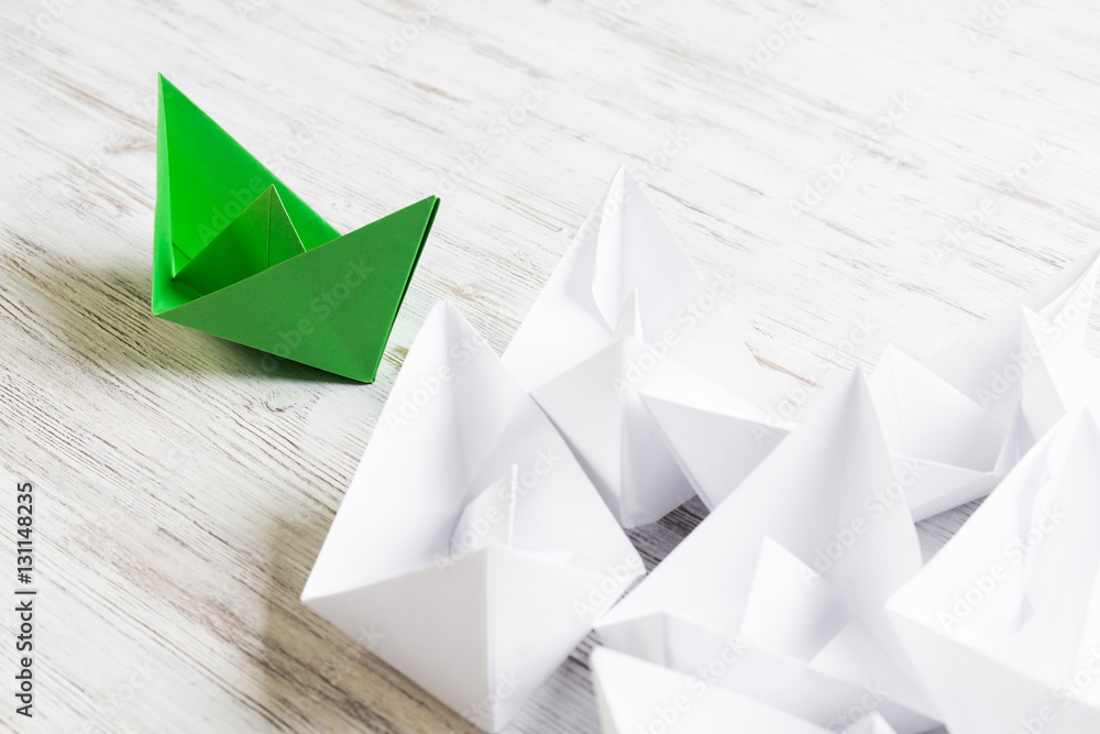 Business leadership concept with white and color paper boats on wooden table