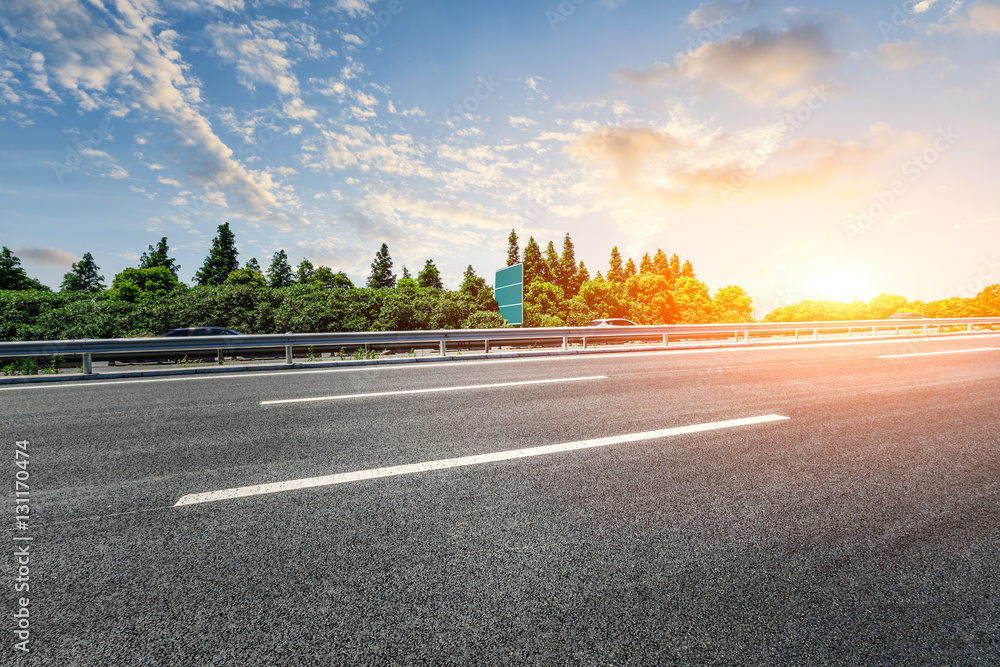 Asphalt road and woods at sunset