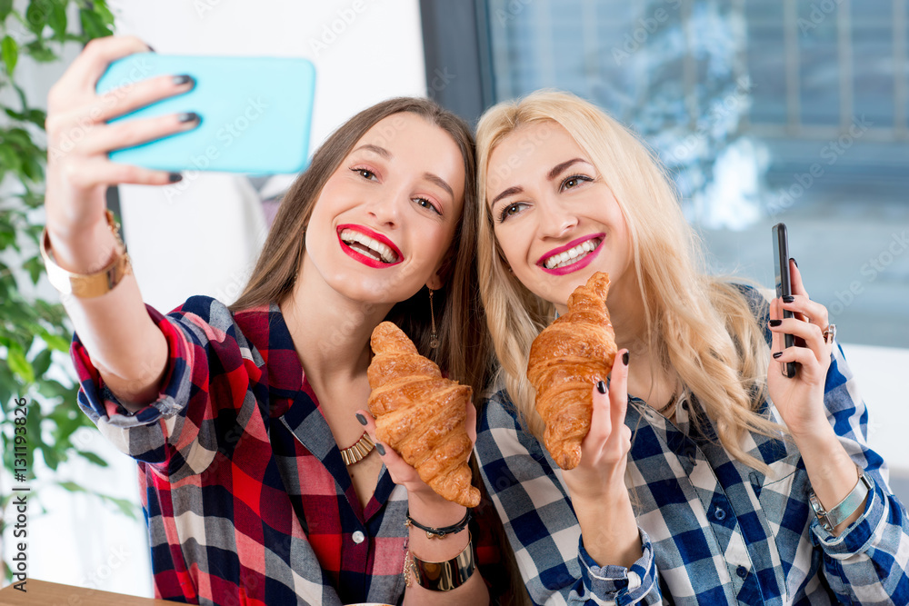 Young female friends dressed casually in checkered shirts taking selfie photo with coffee cups and c