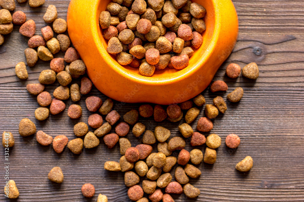 dry cat food in bowl on wooden background top view