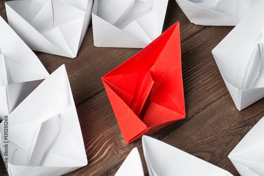 Business leadership concept with white and color paper boats on wooden table