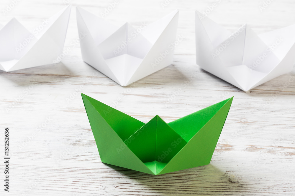 Business leadership concept with white and color paper boats on wooden table