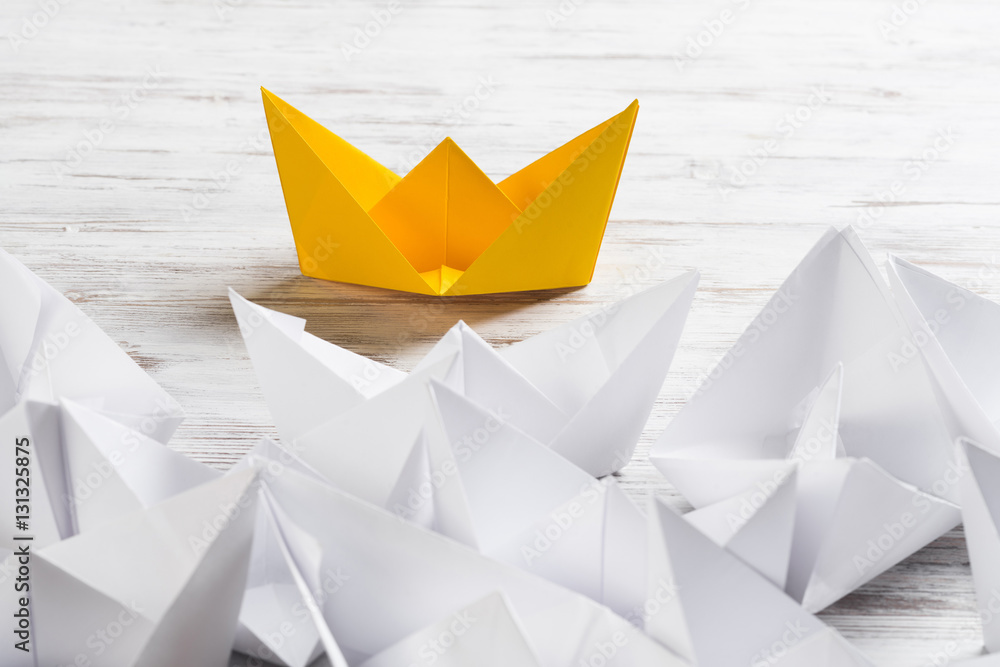 Business leadership concept with white and color paper boats on wooden table