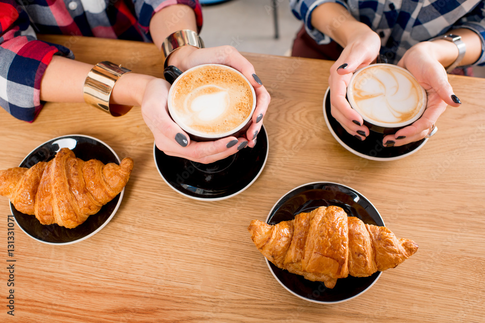 Top view on the wooden table with female hands holding coffee cups and croissants