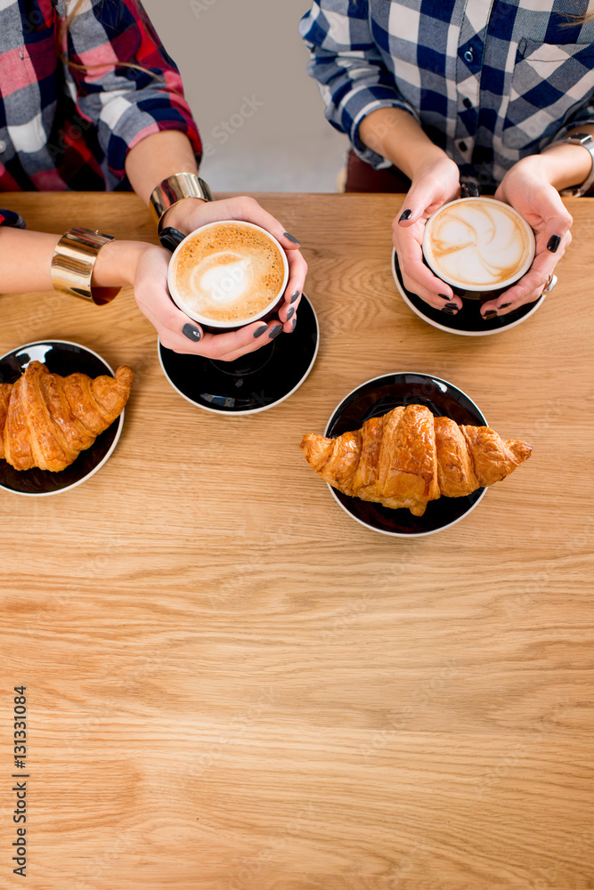 Top view on the wooden table with female hands holding coffee cups and croissants