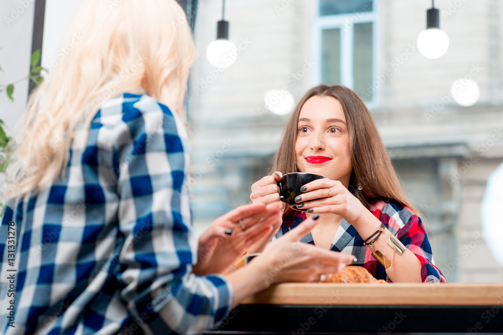 Young female friends dressed casually in checkered shirts sitting with coffee cups and croissants at