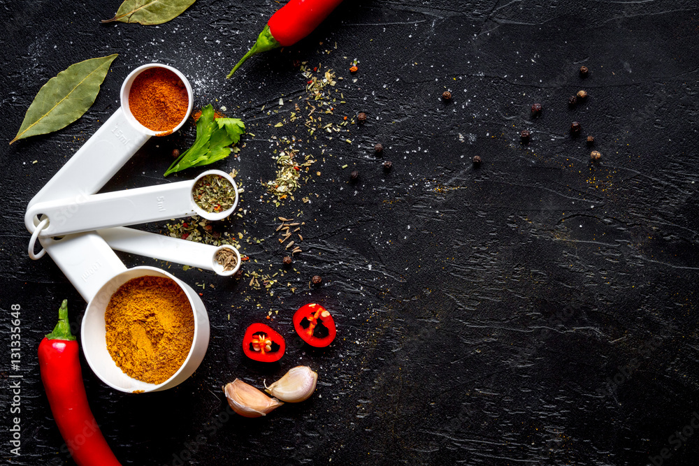 spices in wooden spoons on dark background top view