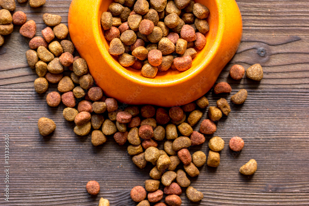 dry cat food in bowl on wooden background top view