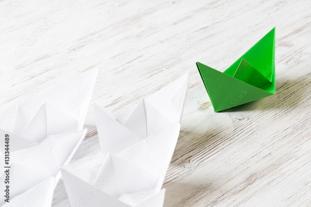 Business leadership concept with white and color paper boats on wooden table