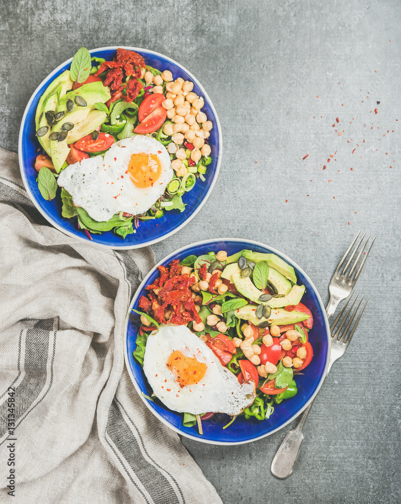 Healthy breakfast bowls with fried egg, chickpea sprouts, seeds, vegetables and greens over grey con