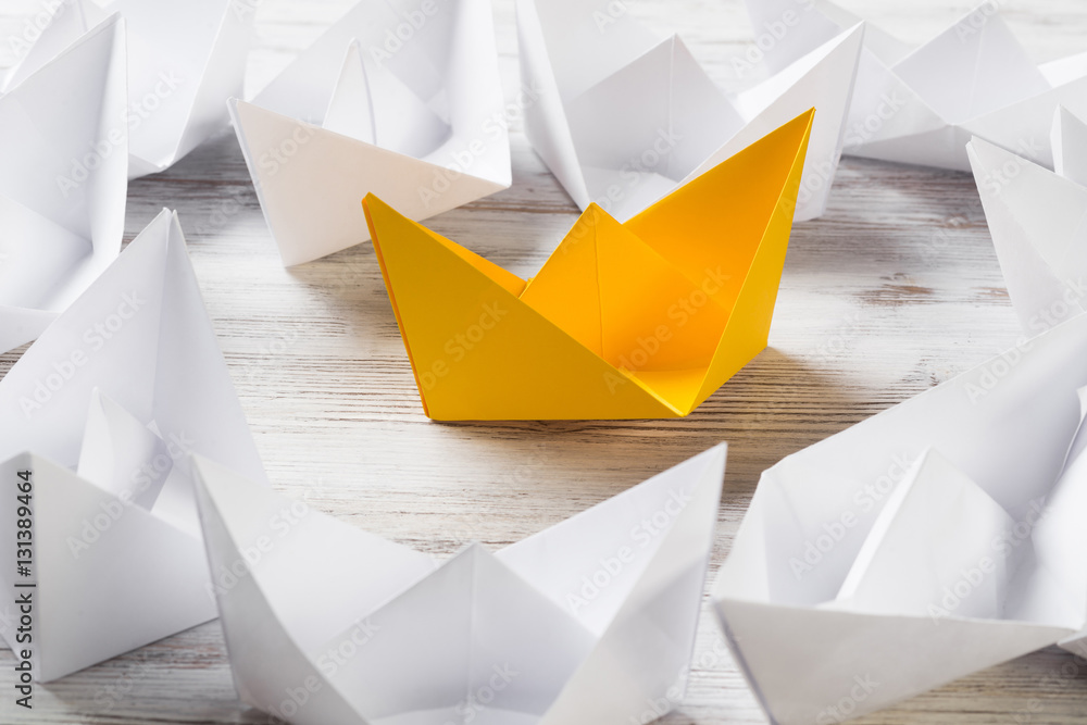 Business leadership concept with white and color paper boats on wooden table