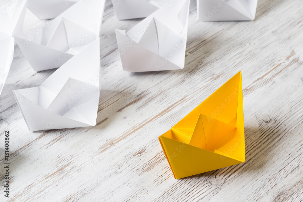 Business leadership concept with white and color paper boats on wooden table