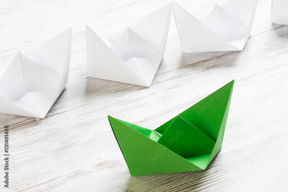 Business leadership concept with white and color paper boats on wooden table