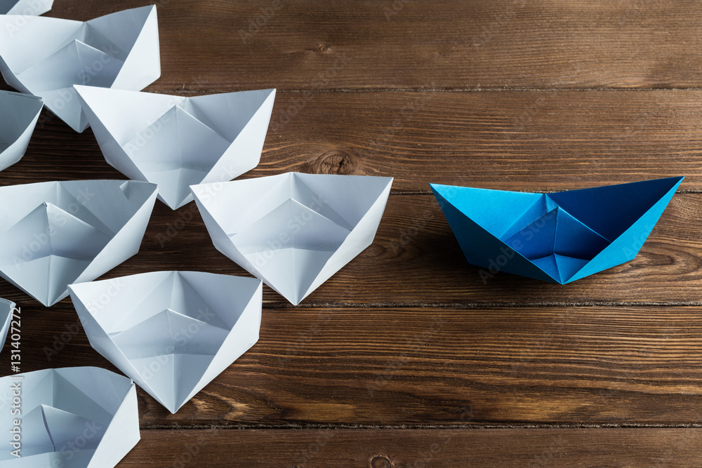 Business leadership concept with white and color paper boats on wooden table