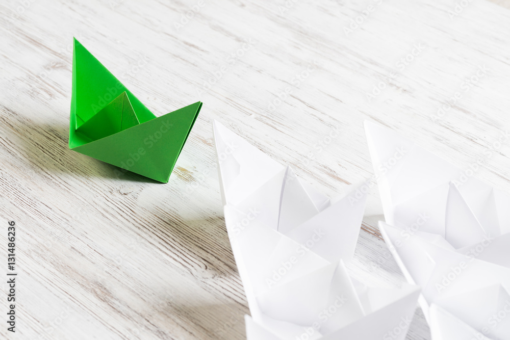 Business leadership concept with white and color paper boats on wooden table