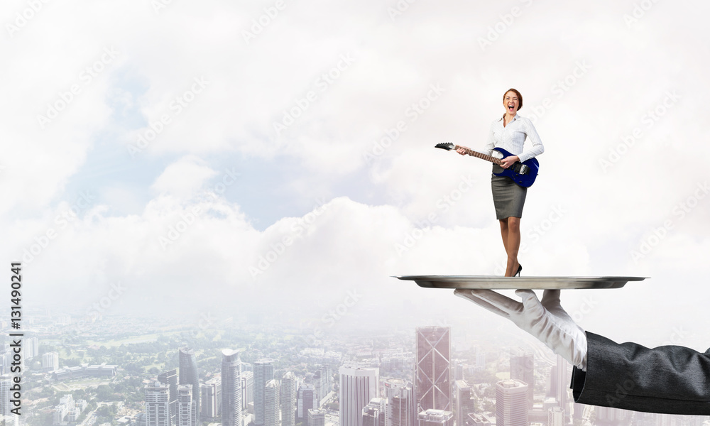 Attractive businesswoman on metal tray playing acoustic guitar against cityscape background