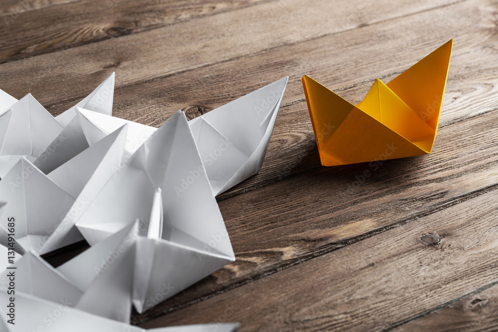 Business leadership concept with white and color paper boats on wooden table