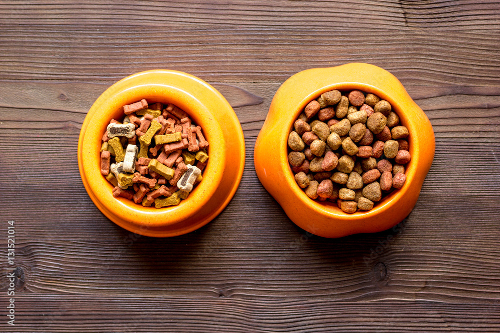 dry dog food in bowl on wooden background top view