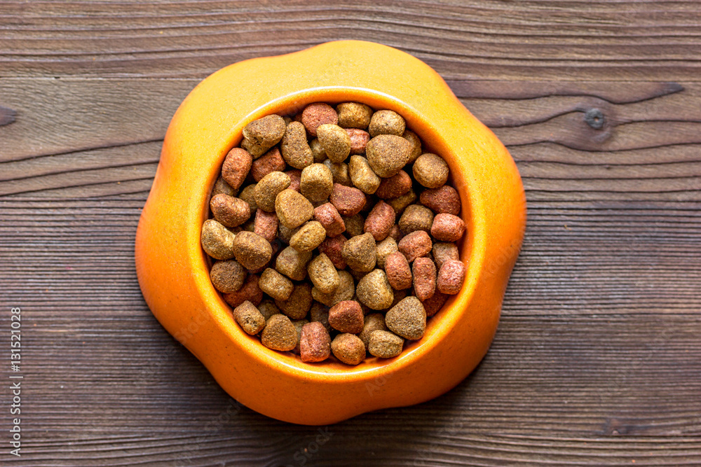 dry cat food in bowl on wooden background top view