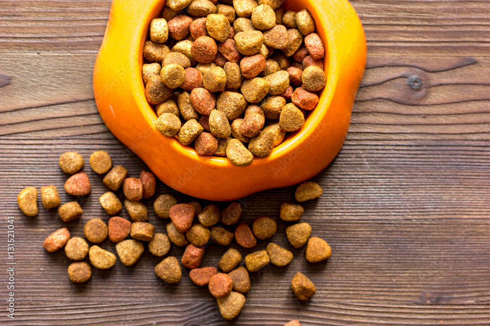 dry cat food in bowl on wooden background top view