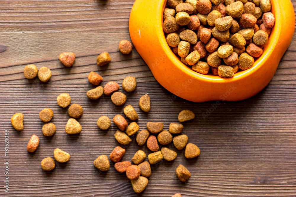 dry cat food in bowl on wooden background top view