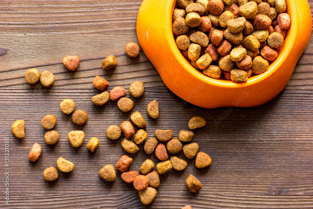 dry cat food in bowl on wooden background top view