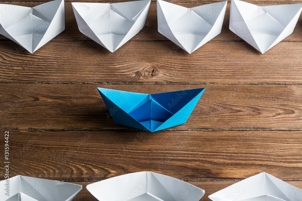 Business leadership concept with white and color paper boats on wooden table