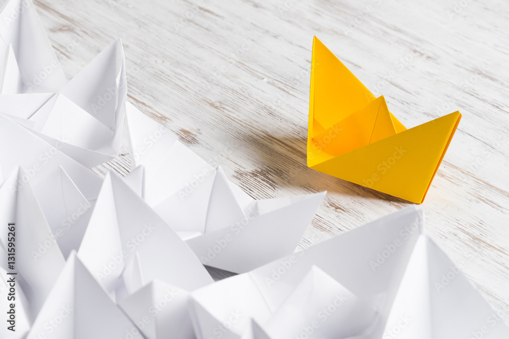 Business leadership concept with white and color paper boats on wooden table