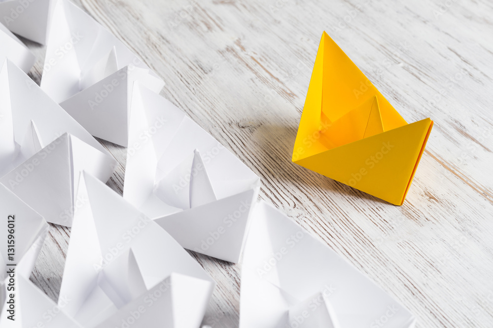 Business leadership concept with white and color paper boats on wooden table