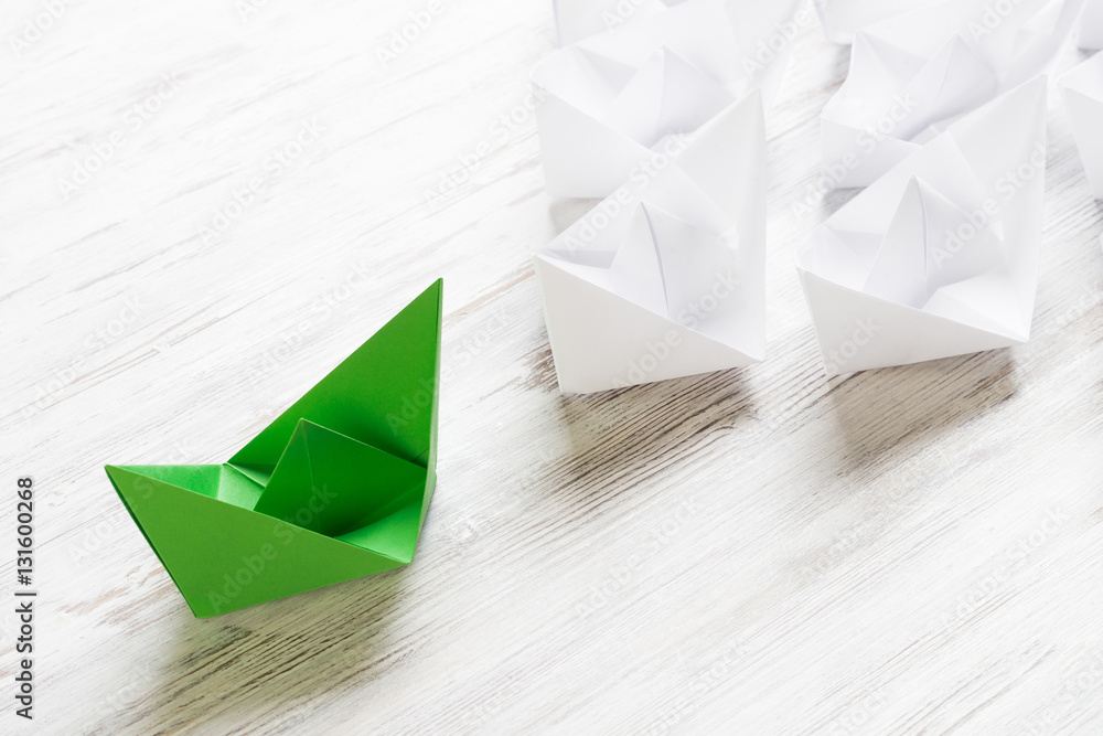 Business leadership concept with white and color paper boats on wooden table