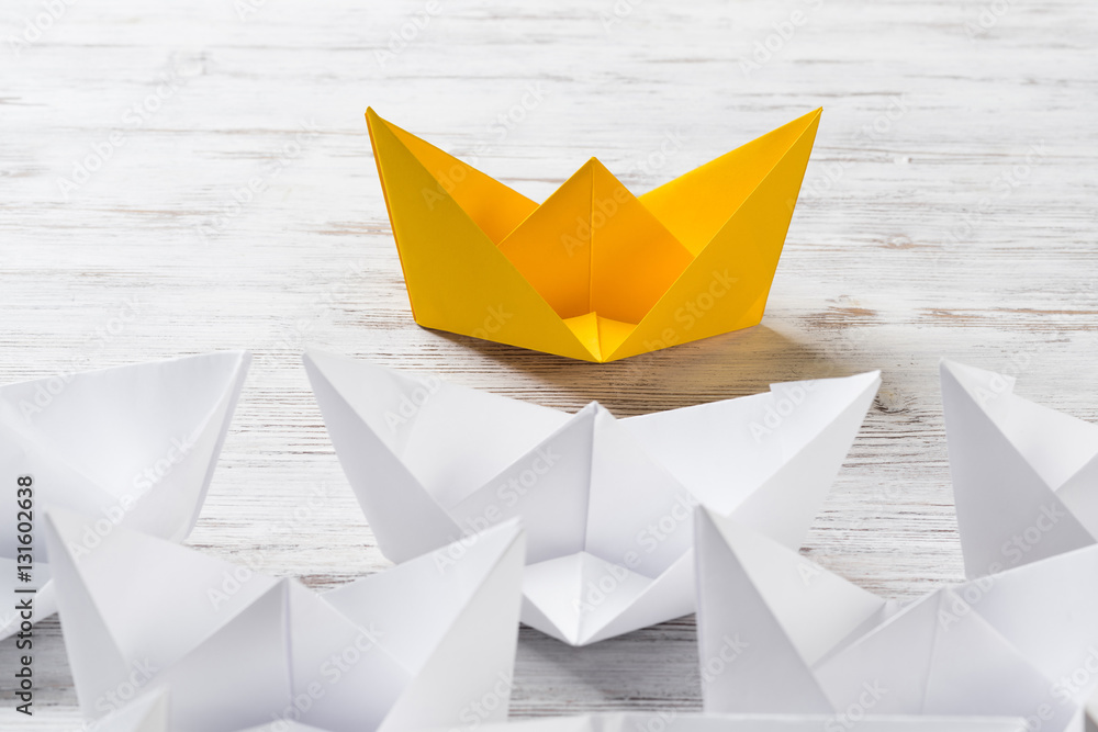 Business leadership concept with white and color paper boats on wooden table