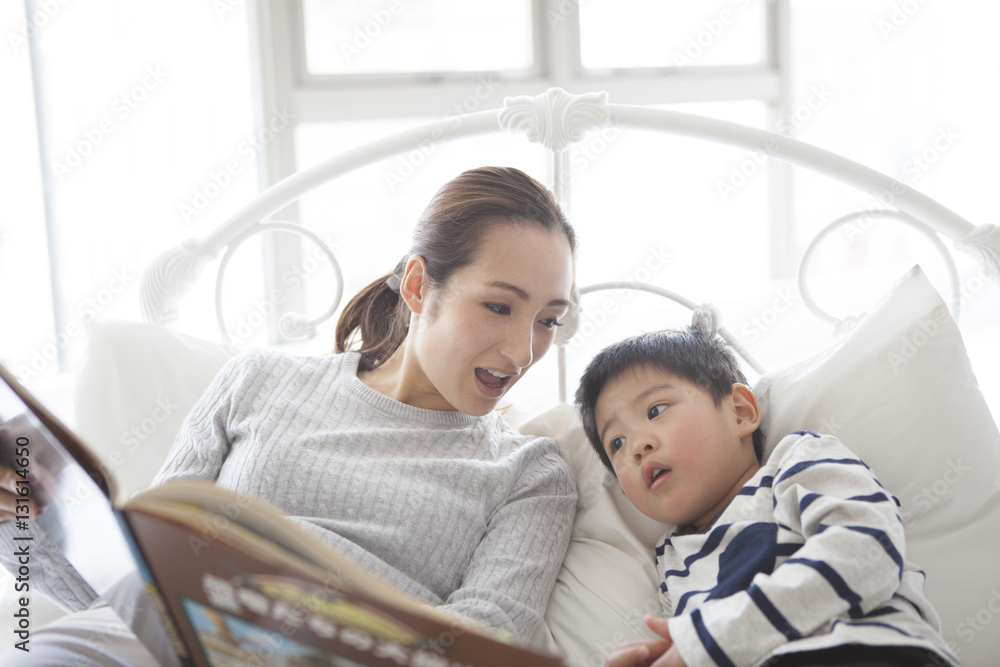 Mother is showing her picture book to her son in bed