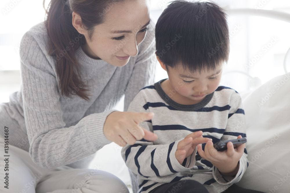 Mother and child are watching smartphone together in the bedroom