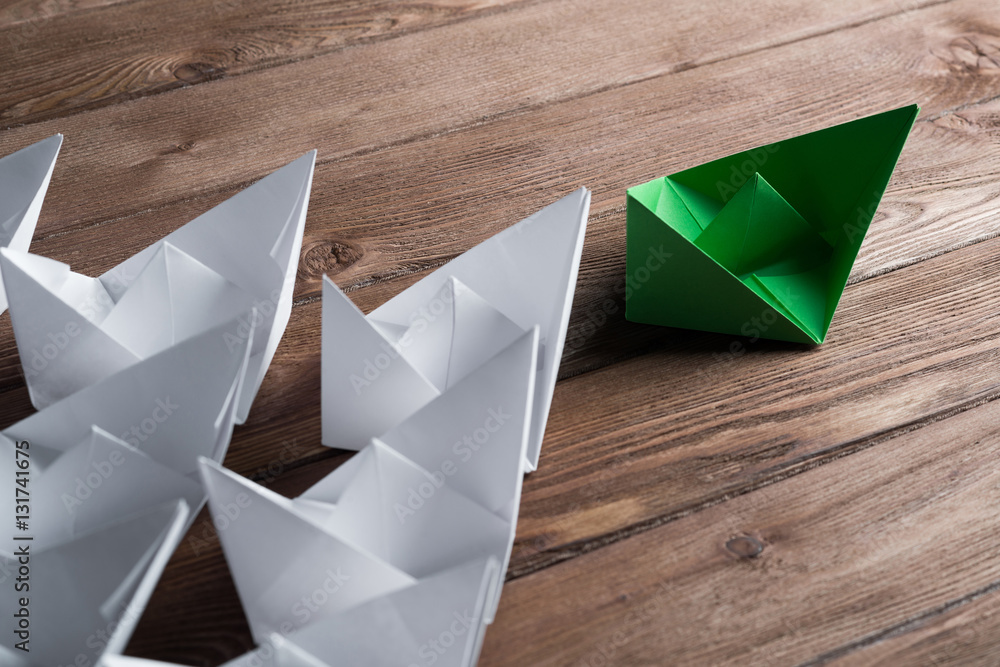 Business leadership concept with white and color paper boats on wooden table