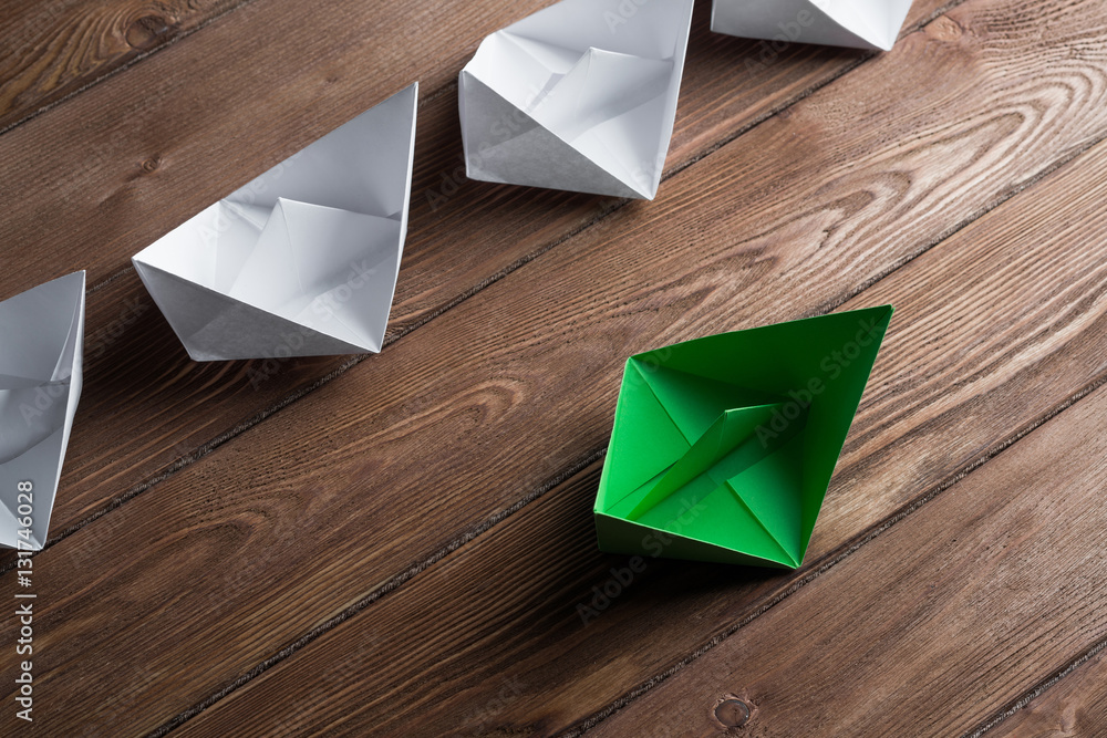 Business leadership concept with white and color paper boats on wooden table