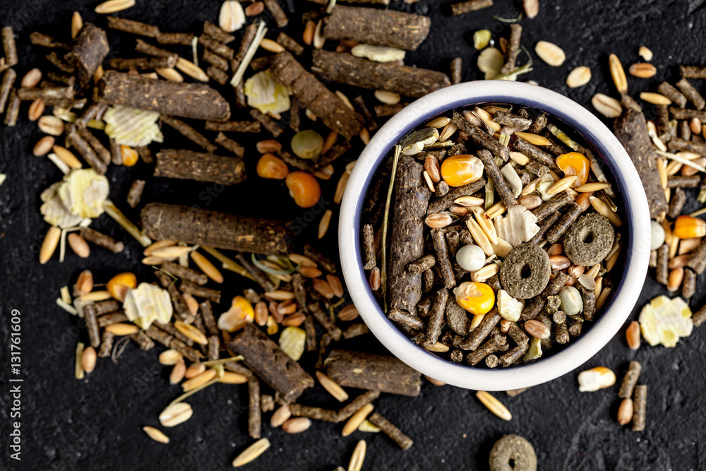 dry food for rodents in bowl dark background top view