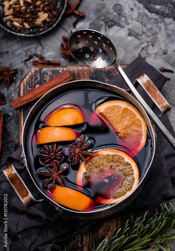 Mulled wine with orange, spices and strainer in aluminum vintage casserole on wooden board. Concrete