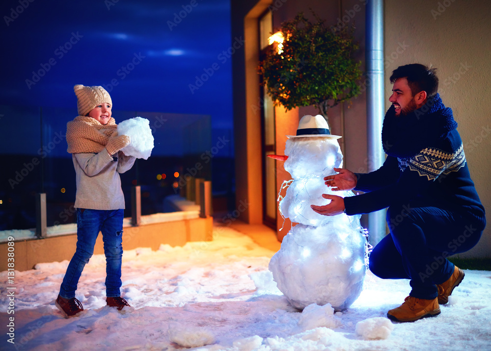 happy father and son making snowman in evening light