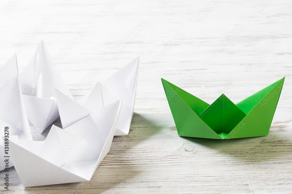 Business leadership concept with white and color paper boats on wooden table