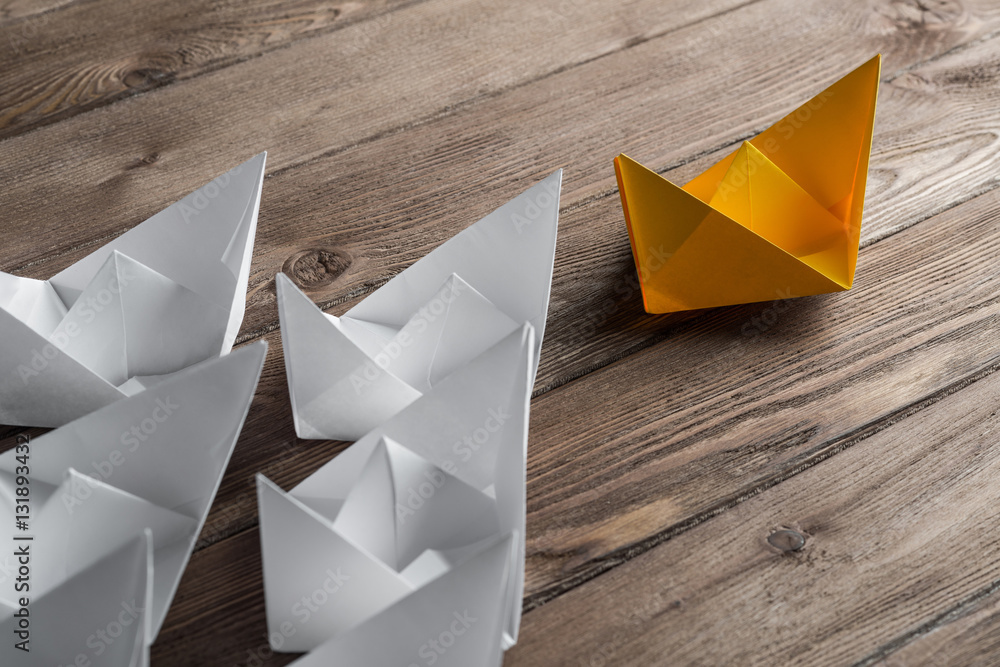 Business leadership concept with white and color paper boats on wooden table