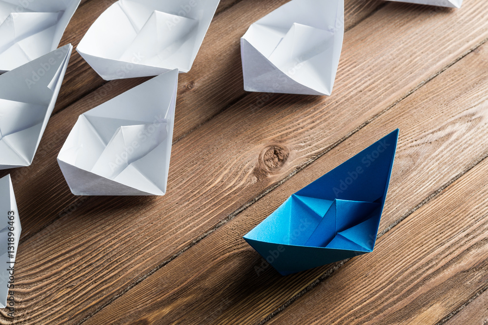 Business leadership concept with white and color paper boats on wooden table